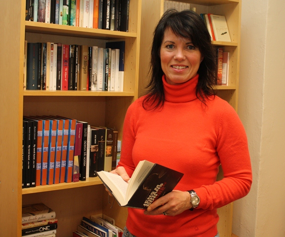 Person med bok framfor bokhylle. Foto.