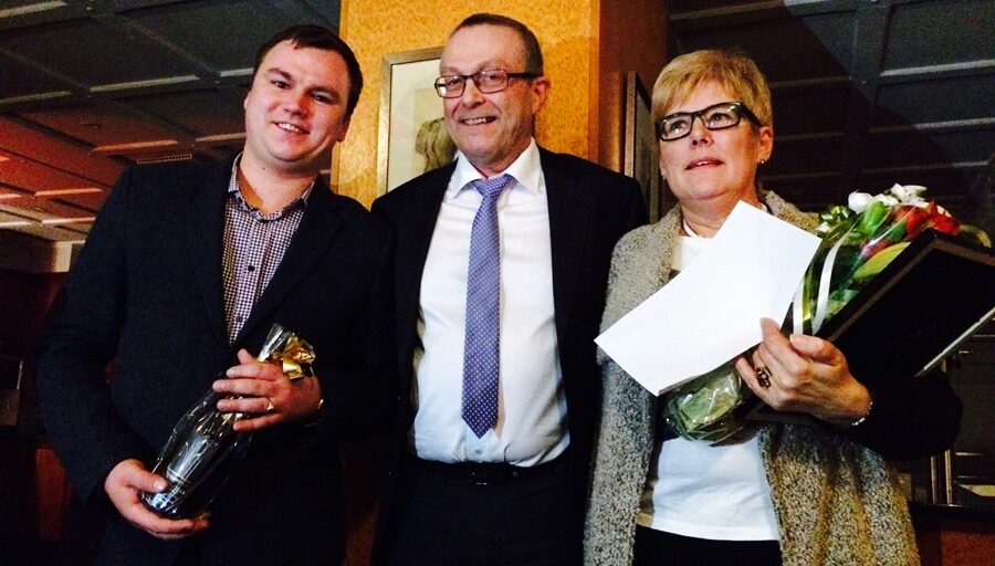3 personar med blomst og diplom. Foto.