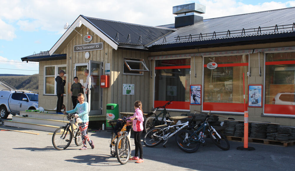To barn med sykkel og tre voksne utenfor butikk.