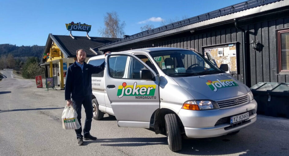 En person med handlepose står ved en bil. Foto.