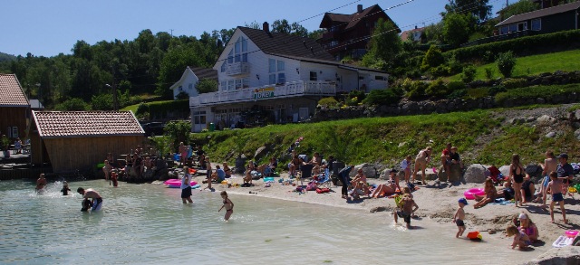 Badestrand med folk som bader. Butikk i bakgrunnen. Foto.