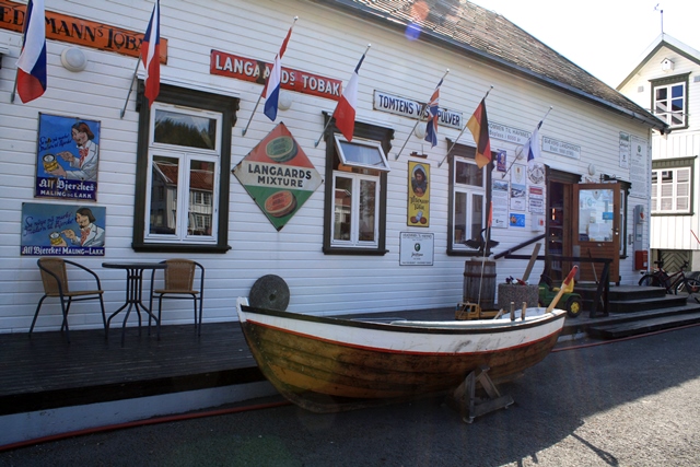 Båt på land utanfor gammal butikk. Foto.