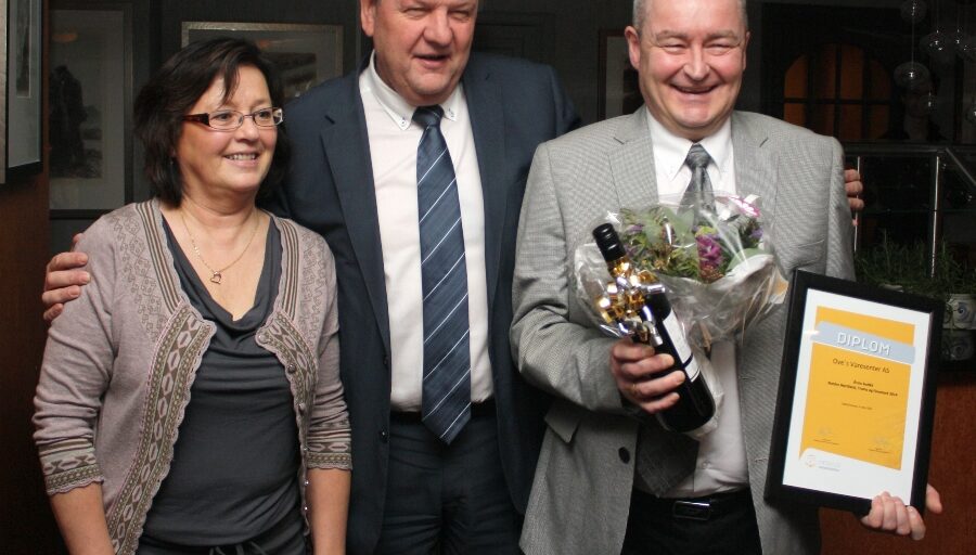 Tre personer med blomst og diplom. Foto.