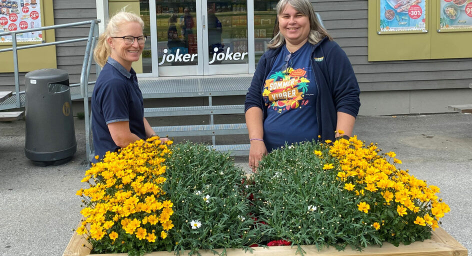 To personar framfor blomsterkasse utanfor inngangen til butikk. Foto.