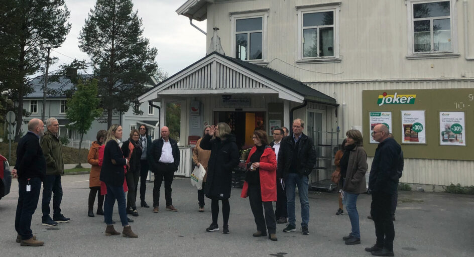 Eg gruppe personer foran butikkbygg. Foto.