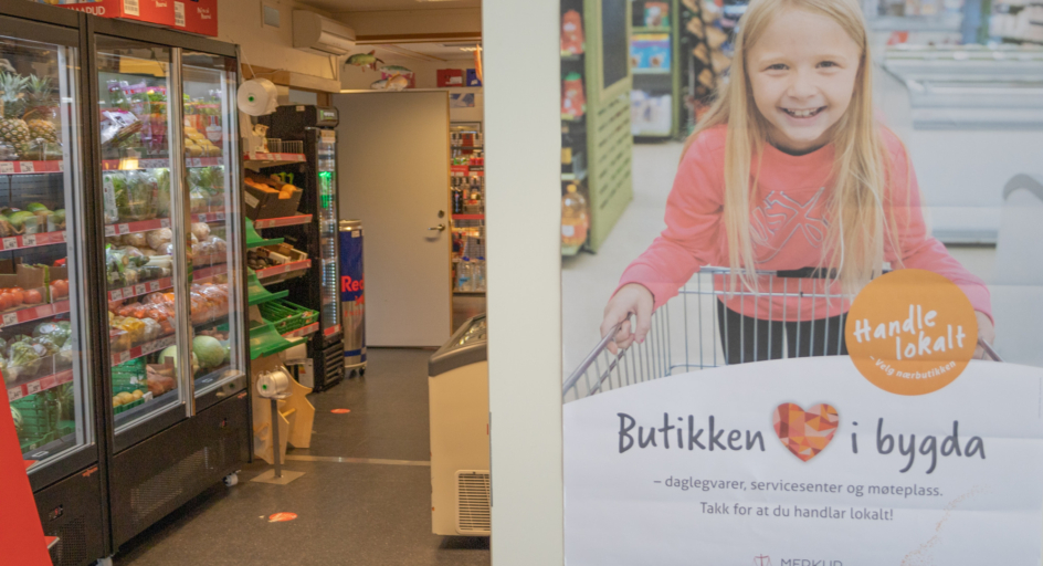 Hyller i ein daglegvarebutikk og ein plakat med teksten Butikken i bygda i framgrunnen.