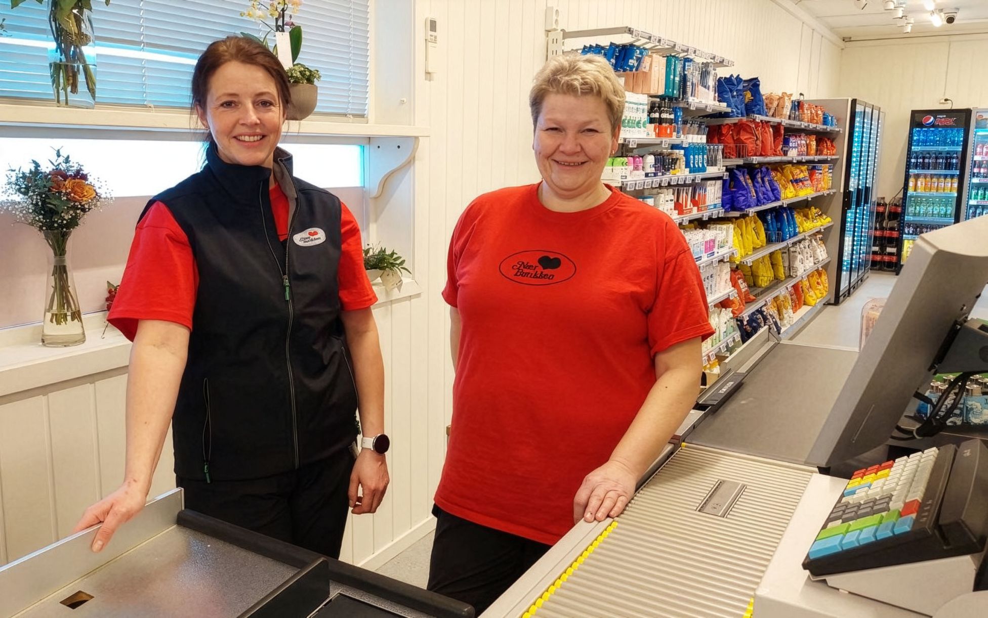 To kvinner som står bak kassen i en dagligvarebutikk