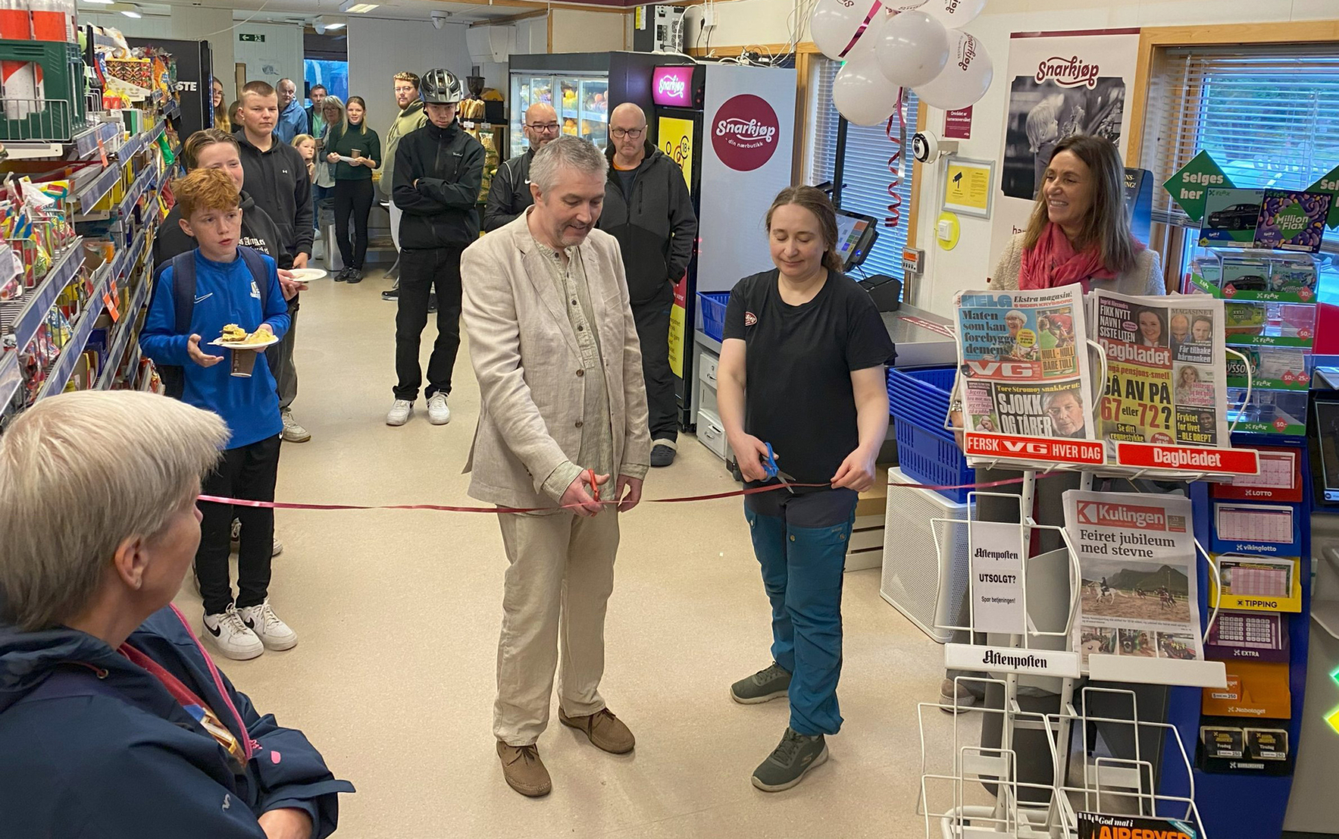 En gruppe mennesker som står i en butikk. Klipping av snor.